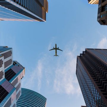 Airplane flies over Chicago's modern skyscrapers against a clear sky, highlighting urban architecture.